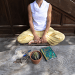 Mujer en meditación con cuaderno y planta, un gesto sencillo como ritual de regreso a sí misma".