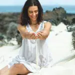 Mujer dejando caer arena entre sus manos sobre la playa, símbolo del arte de no hacer y de la calma que surge al soltar y confiar en la vida.